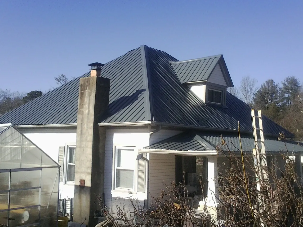 Dark blue standing seam metal roof on a white farmhouse with dormer — Slate & Tile Roof Repair by Roofing Brothers in Strongstown