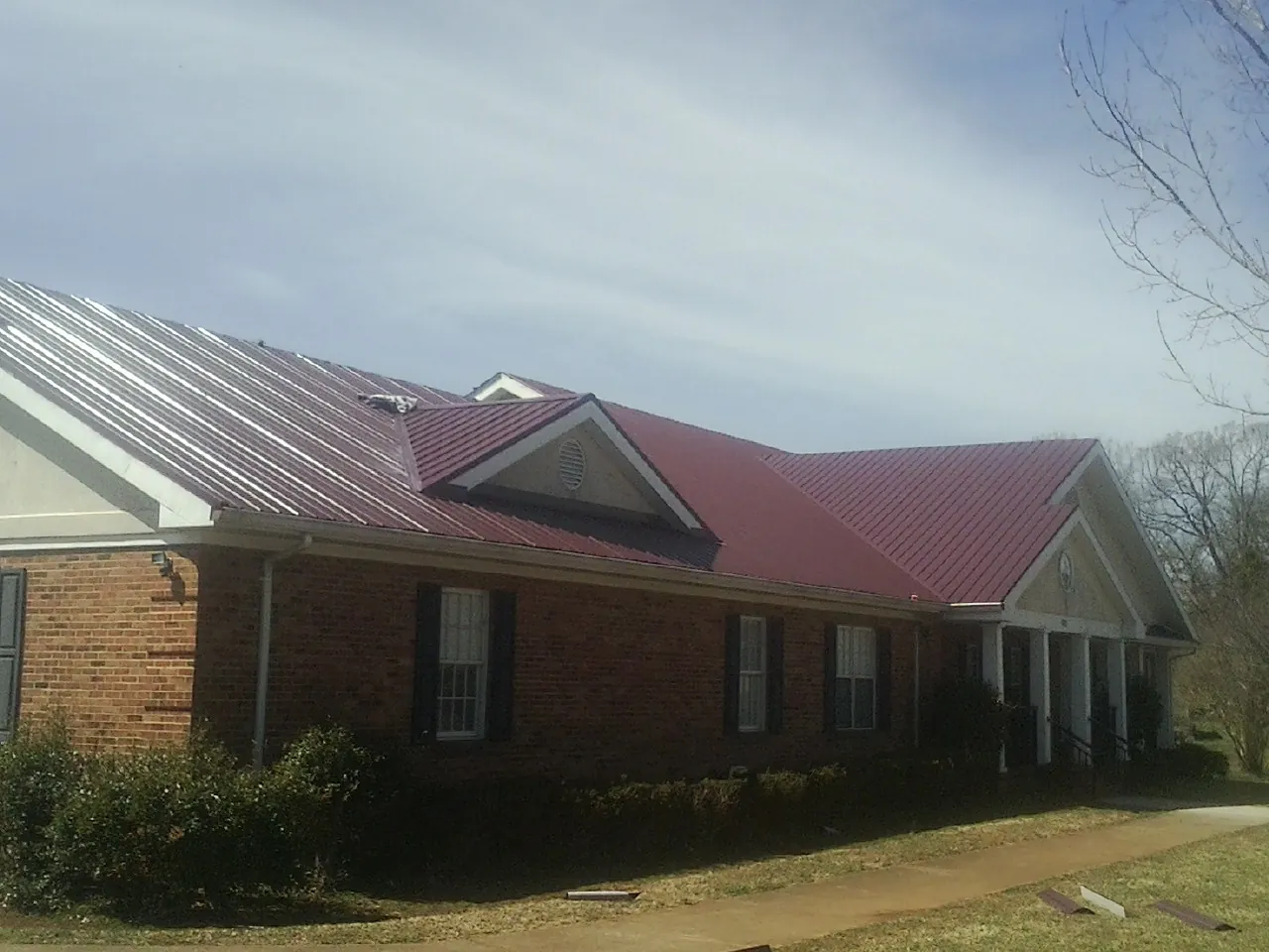 Red metal roof with gabled entries on a long brick building, from a Hail Damage Roof Repair job in Strongstown