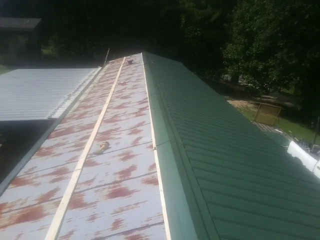 Old rusted panels beside newly installed green metal roofing — Wind Damage Roof Repair by Roofing Brothers in Strongstown