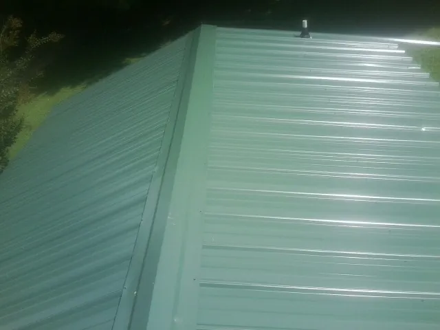 New green metal panels meeting at the ridge of a roof — Flat Roof Repair work by our crew in Strongstown