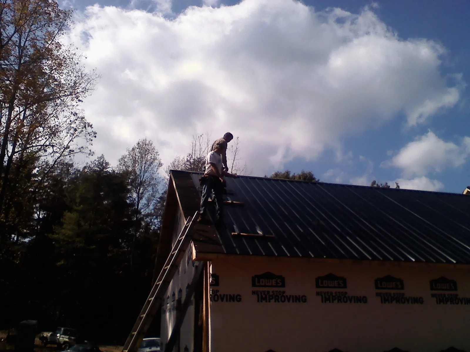 Roofer fastening dark metal panels high against a cloudy sky, from a Roof Inspection job in Strongstown