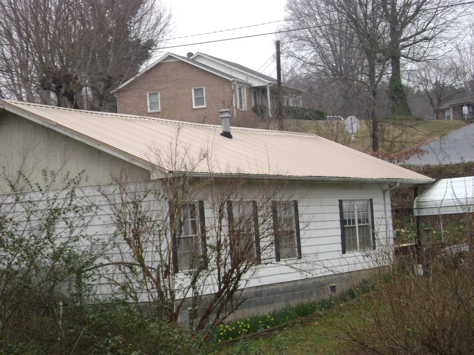 Tan metal roof on a white sided house set into a hillside in Strongstown