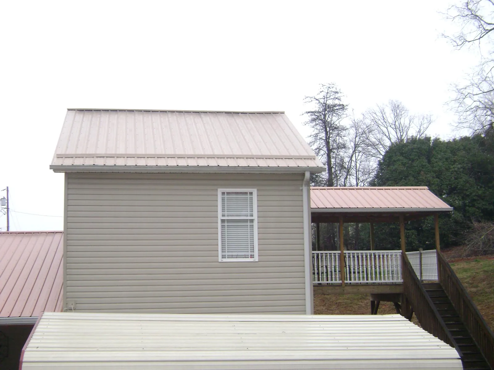 Tan metal roofs on a two story addition and attached porch, from a Roof Replacement job in Strongstown
